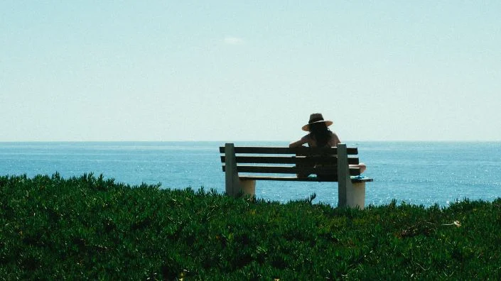 Žena sjedi na klupi pored mora
