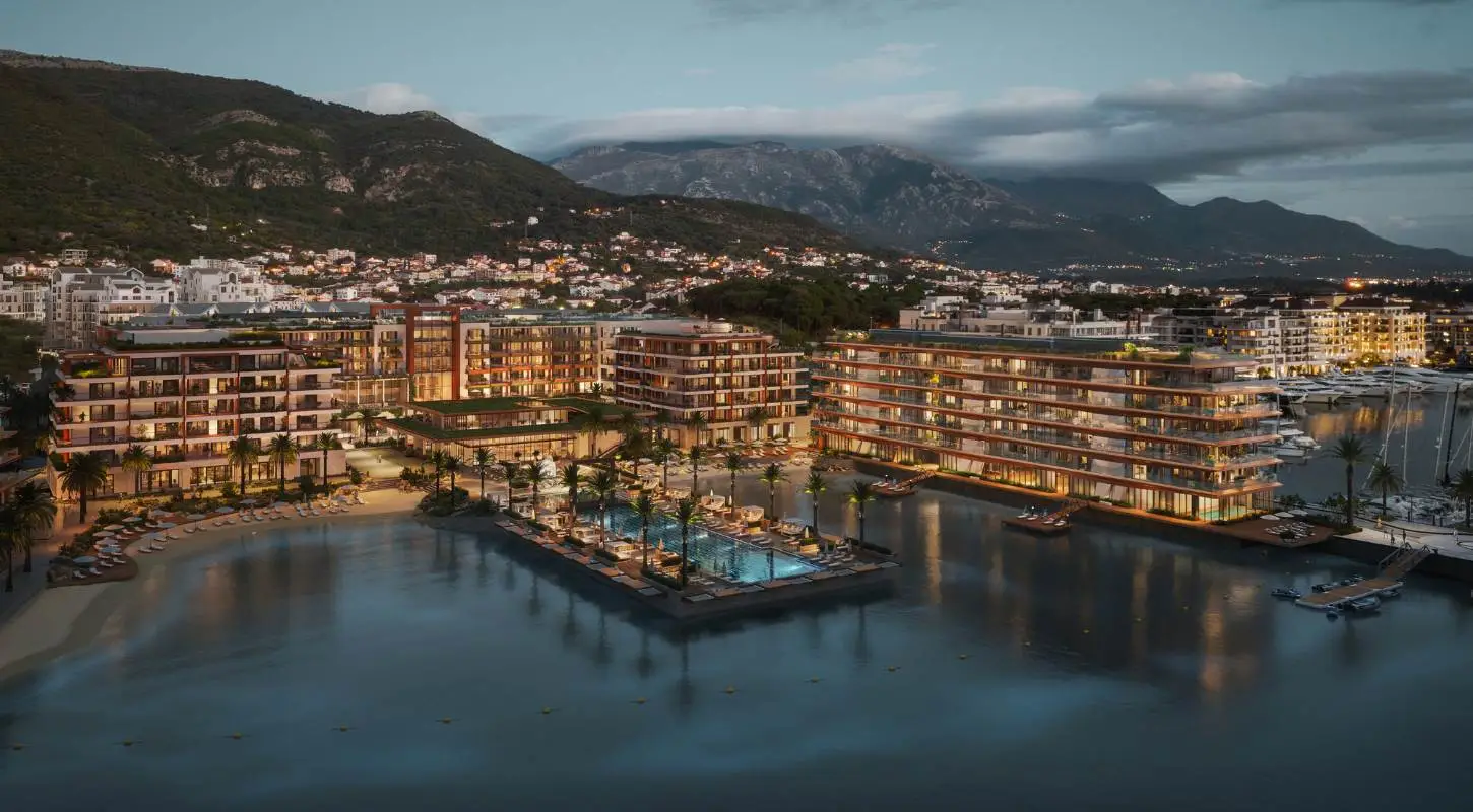 Night view of Synchro Yards, showcasing the illuminated AERIS residence with waterfront reflections and a mountain backdrop.