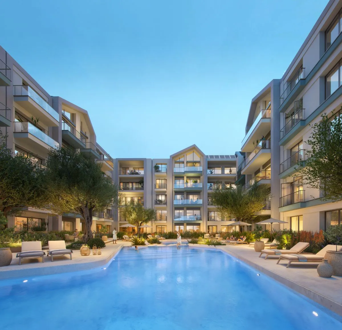 Serene courtyard pool at Vero and Versa illuminated at dusk, surrounded by modern apartments, olive trees, and relaxed seating-offering a calming ambiance as the evening unfolds.