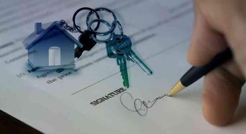 Close-up of a person signing a property purchase contract with a small house model and a SOLD sign, symbolising buying property abroad.