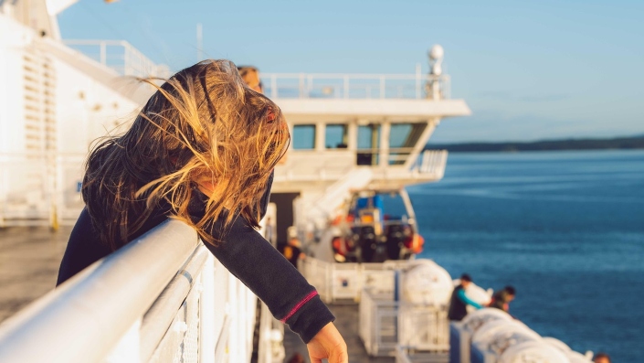 A child standing at the railing of a ferry, looking out over the sea as the ship moves forward.