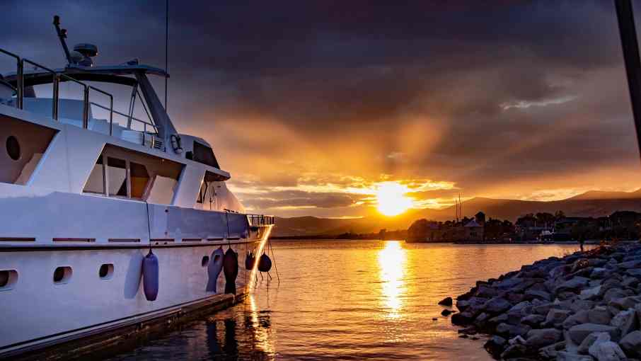 Single white yacht with gentle swell and a low sun near the horizon, warm golden light.