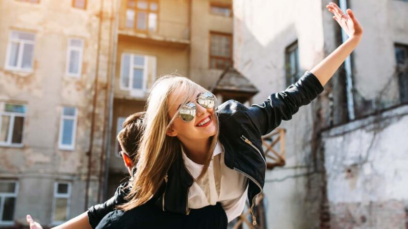 Girl joyfully lifted in her boyfriend’s arms in a sunny city, enjoying beautiful weather.