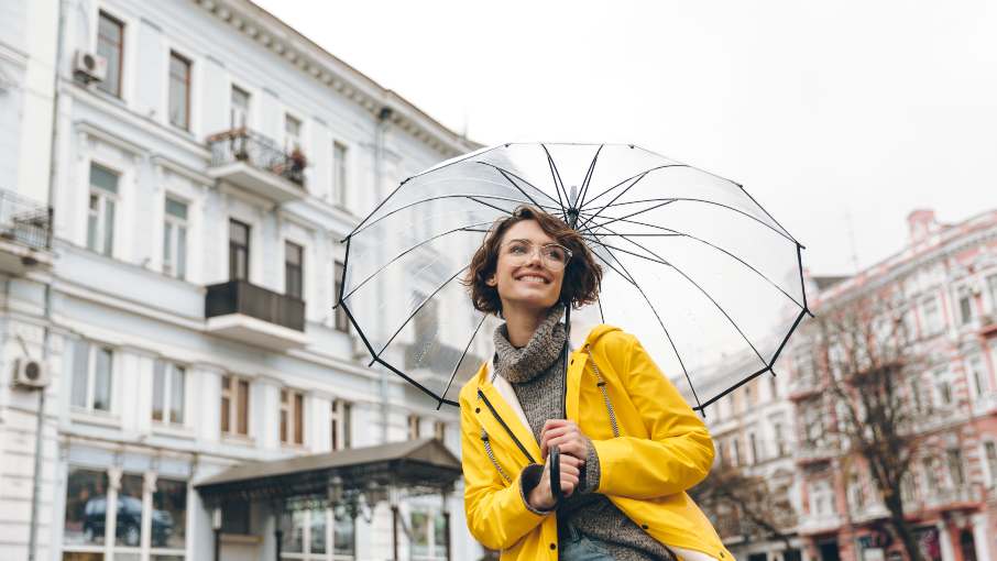 Woman in yellow raincoat holding a large transparent umbrella.