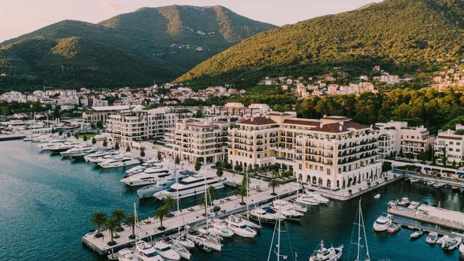 Aerial view of Hotel Regent Porto Montenegro with yachts docked in the marina and green hills in the background.