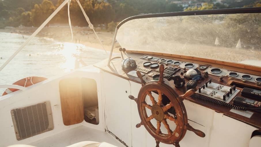 Wooden yacht helm glowing in the sun above a calm sea.