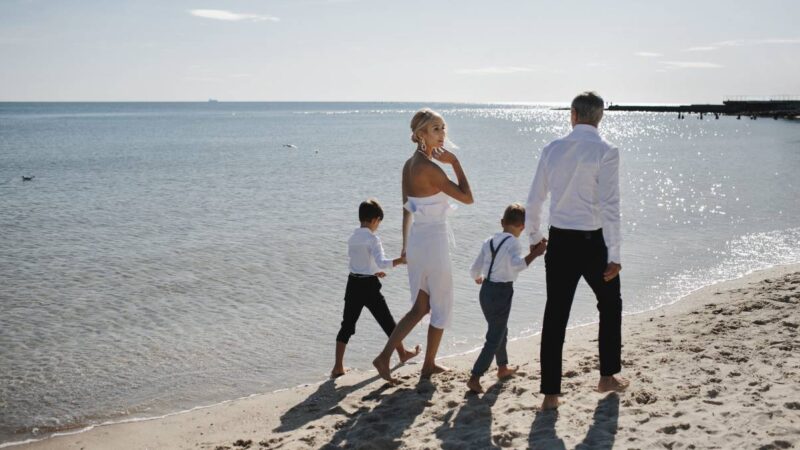 Family walking barefoot on a sandy beach during a luxury holiday in Europe.