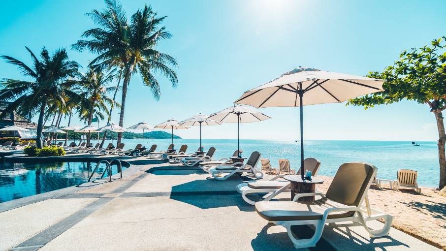 Luxury resort swimming pool with sun umbrellas, palm trees and sea views.